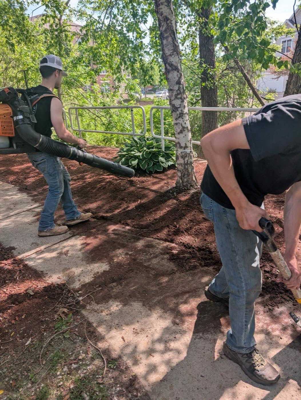 Crew clearing debris from a sidewalk by hand and blower
