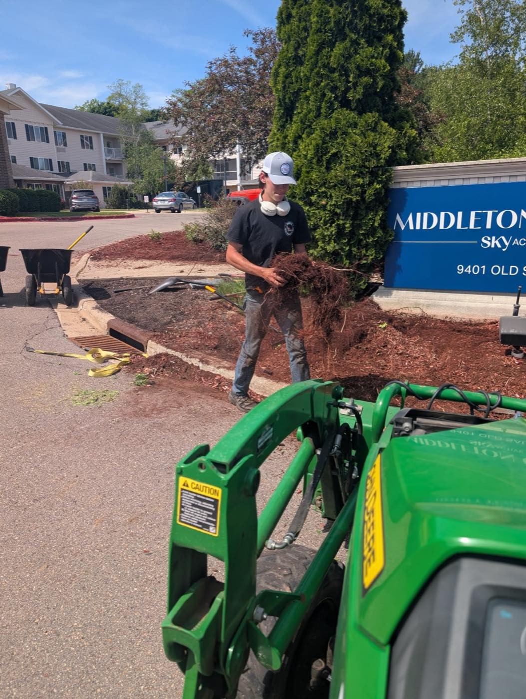 Crew member gathering mulch near a commercial property sign