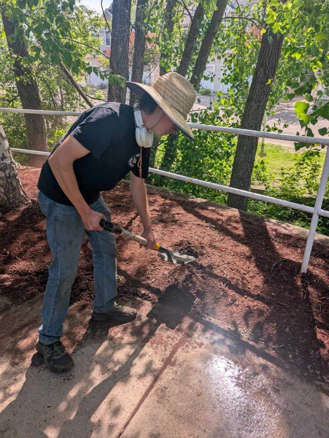 Crew member spreading mulch along a fenced walkway